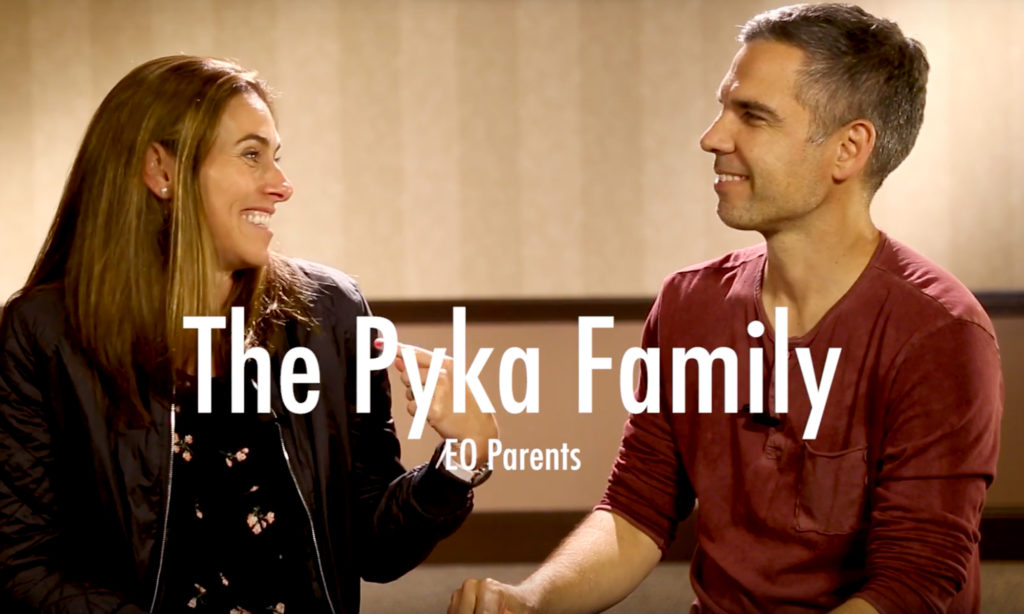 A married couple are being interviewed, looking at each other with the words, "The Pyka Family, EO Parents" on screen